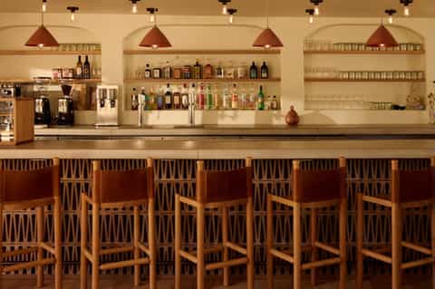 Upscale bar with wooden chairs, copper pendant lights, and shelves stocked with spirits and glassware