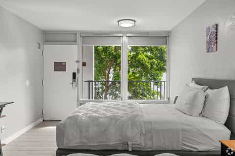 Bright hotel bedroom with modern furnishings and sliding glass door overlooking trees and balcony