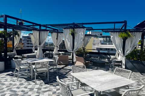 Rooftop terrace with pergola, white curtains, lounge seating, and city views