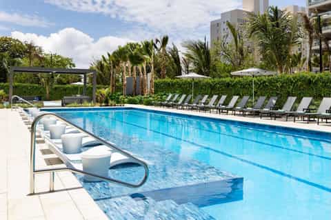 Resort lap pool with diving platform, white umbrellas, loungers, and palm tree landscaping