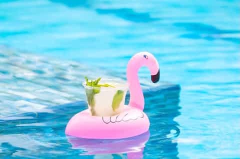 Pink flamingo pool float holding a cocktail in bright blue resort swimming pool