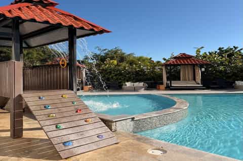 Resort pool with climbing wall, gazebos with red roofs, and tropical landscaping