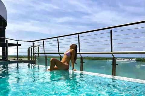 Rooftop infinity pool with person relaxing, cable railings, panoramic countryside views, and modern architecture