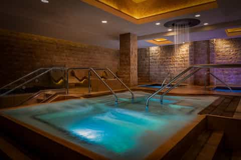 Underground spa with hot tubs, stone walls, warm accent lighting, and handrails for safety