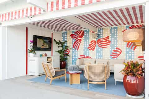 Retro-style resort lounge with striped awning, colorful wallpaper, and mid-century furniture