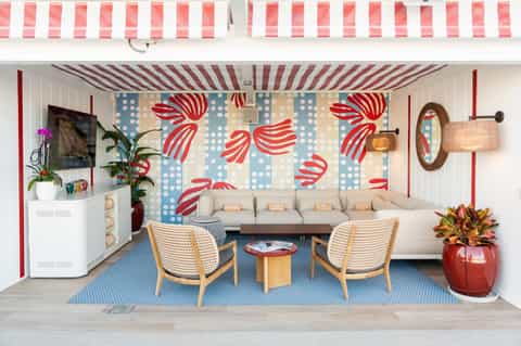 Colorful beach-themed cabana interior with striped awning, sofa, wicker chairs, and nautical decor
