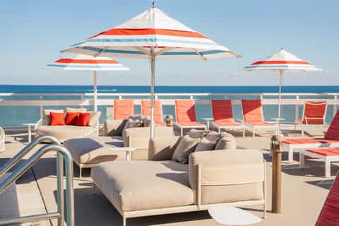 Oceanfront deck with lounge seating, red and white striped umbrellas, and sea views