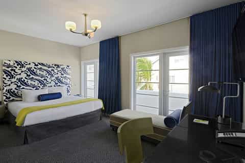 Hotel bedroom with navy and lime accents, patterned headboard, balcony access, and modern furnishings