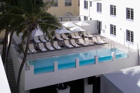 Modern resort pool area with loungers, white umbrellas, palm trees, and contemporary white building
