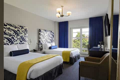 Hotel room with two beds, navy blue decorative headboards, yellow bed runners, and blue curtains