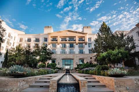 Elegant hotel courtyard with white and tan facade, manicured gardens, succulent plantings, and water feature.