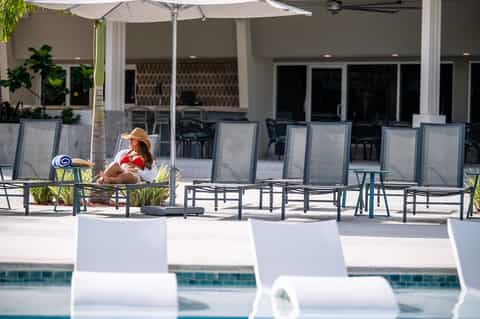 Resort pool deck with lounge chairs, umbrellas, and guests relaxing poolside
