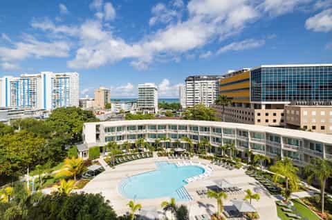 Aerial view of curved pool with lounge chairs surrounded by palm trees and hotel buildings