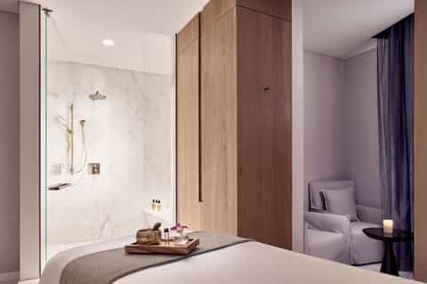 Luxury bathroom with marble walk-in shower, wood vanity, and separate seating area with purple chair