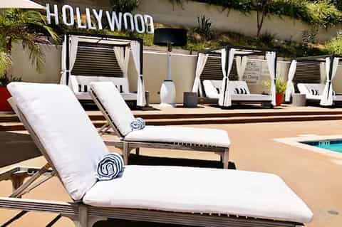 Luxury poolside lounge chairs with white cushions and rolled towels under the Hollywood sign
