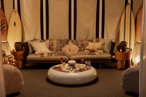 Lounge area with coastal decor, surfboards, leather sofa, and round white ottoman with snacks