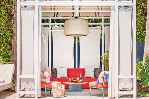 Modern cabana with red cushioned seating, white drapes, and pendant lighting