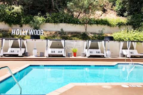 Resort pool with white cabanas and Hollywood sign visible on hillside behind property