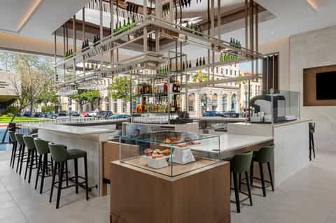 Modern hotel bar with glass wine display, wood and metal shelving, bar seating, and city view