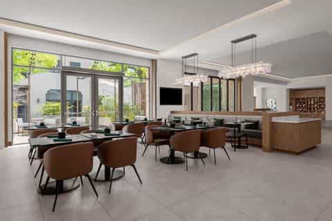 Contemporary hotel lobby with dining area, earth-tone seating, crystal chandeliers, and large windows