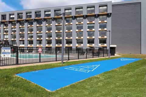 Contemporary multi-story hotel building with metal framework, large windows, and cornhole court on lawn