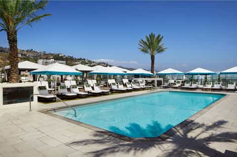 Resort rooftop pool with blue water, turquoise umbrellas, white loungers, and mountain views