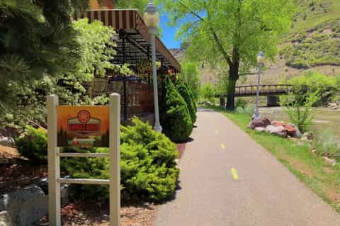 Riverside resort entrance with signage, wooden stairs, lush landscaping, and mountains in background