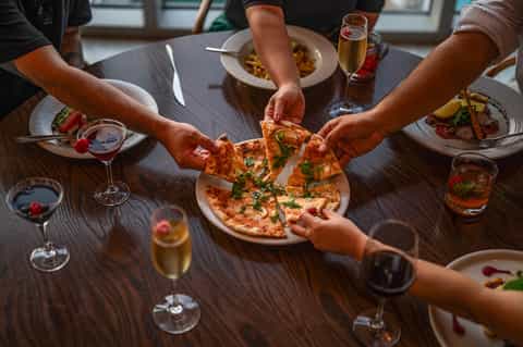 Overhead view of diners sharing pizza and wine at restaurant table with plated food