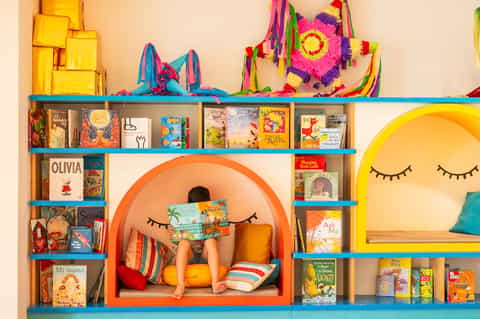 Colorful children's reading nook with orange alcove, shelves of books, and decorative hanging ornaments