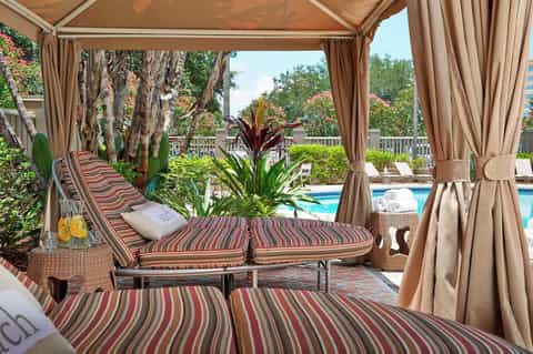 Luxurious poolside cabana with striped loungers, sheer curtains, tropical plants, and pool view
