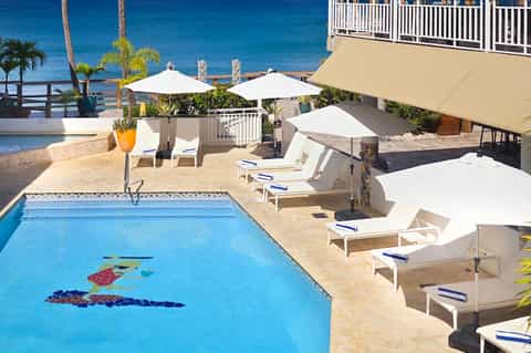 Beachfront pool with decorative fish mosaics, white lounge chairs, umbrellas, and ocean backdrop