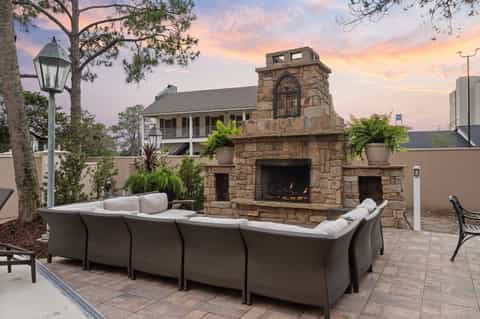 Outdoor patio with curved seating, stone fireplace, ocean views, and evening sunset lighting.