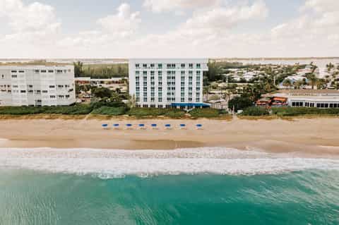 Beachfront resort building with white facade and blue umbrellas on sandy beach with ocean waves