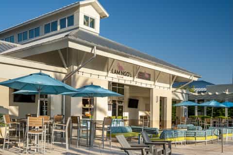 Casual beachside restaurant with blue umbrellas, outdoor seating, and sand dune access