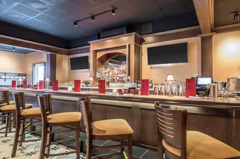Hotel bar with dark wood counter, red accents, and multiple television screens