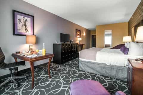 Hotel room with two beds, desk, TV, and purple and gold color accents