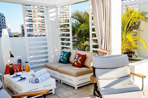 Modern rooftop terrace with lounge seating, potted palm plants, colorful pillows, and city views