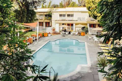 Residential courtyard pool surrounded by lush greenery, orange lounge chairs, and two-story buildings