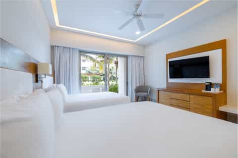 Luxury resort bedroom with two queen beds, ocean view balcony, and wooden furnishings