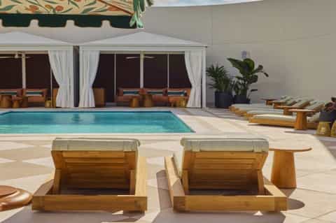 Luxury poolside cabana with wooden sun loungers, cabana seating, and covered lounge area by turquoise pool