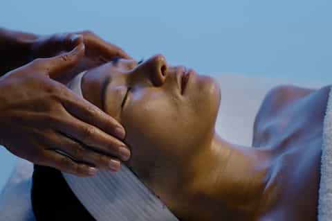 Close-up of facial massage being performed on relaxed client outdoors against blue sky