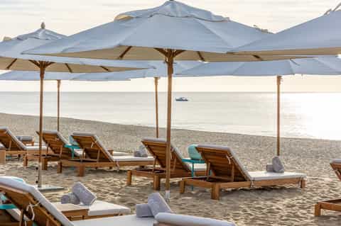 Beach cabanas with blue umbrellas, wooden loungers with cushions, and ocean view