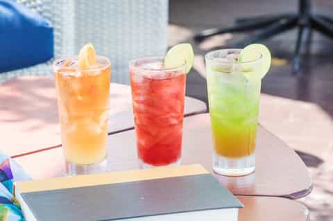 Three colorful cocktails with citrus garnishes on outdoor patio table