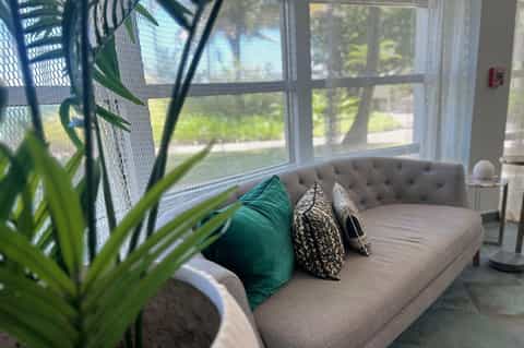 Beige tufted bench with decorative pillows near large windows overlooking grounds