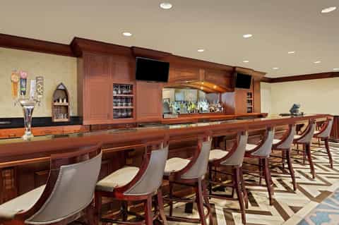 Upscale wooden bar with extensive liquor selection, bar seating, and polished mahogany countertop