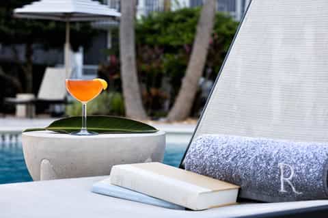 Poolside cocktail on concrete table with lounge chair and tropical resort setting in background