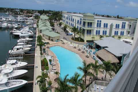 Waterfront resort aerial view with swimming pool, marina with boats, palm trees, and blue-roofed buildings