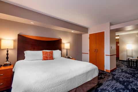Hotel bedroom with burgundy headboard, queen bed, warm lighting, orange accents, and modern furnishings