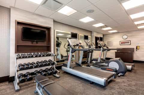 Fitness center with cardio equipment, weights, dumbbells, and TV monitor