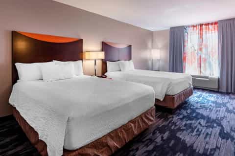 Hotel bedroom with two queen beds, burgundy headboards, blue patterned carpet, and coral curtains